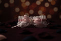 Lace bow with pink ribbon and pearl decorations on a wooden surface with flowers.