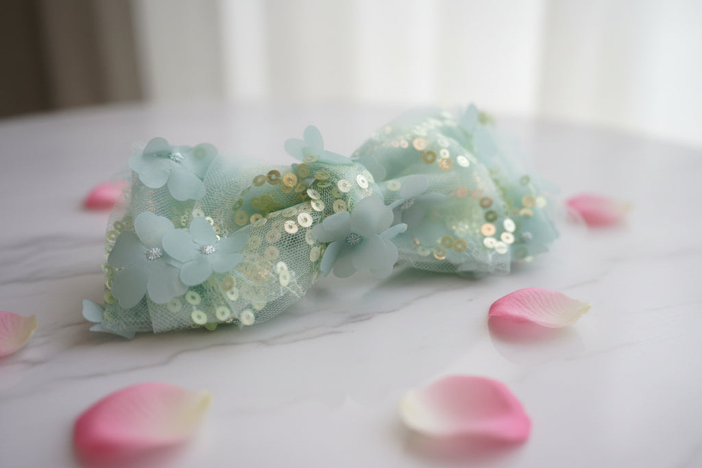 Light blue bow with sequins on a wooden surface with flowers.