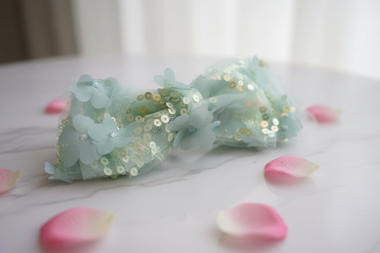Light blue bow with sequins on a wooden surface with flowers.